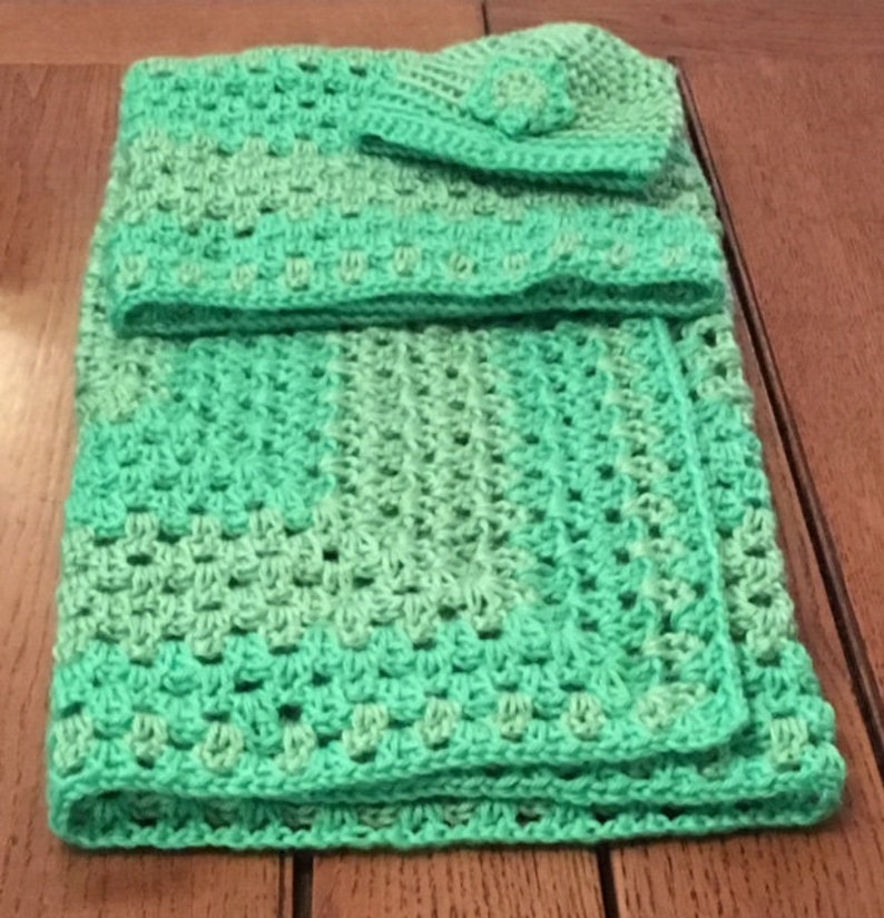 May include: A green crocheted baby blanket with a matching hat. The blanket is made with a textured stitch and has a gradient of green shades.