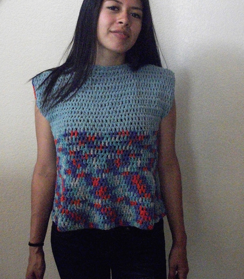 May include: A blue crocheted sleeveless top with a geometric pattern in shades of blue, red, and white.