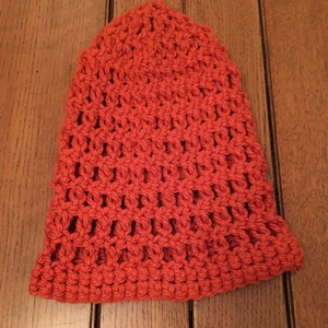 Puede incluir: Un gorro de punto de ganchillo de color naranja brillante. El gorro tiene un patr&oacute;n de punto simple y abierto.