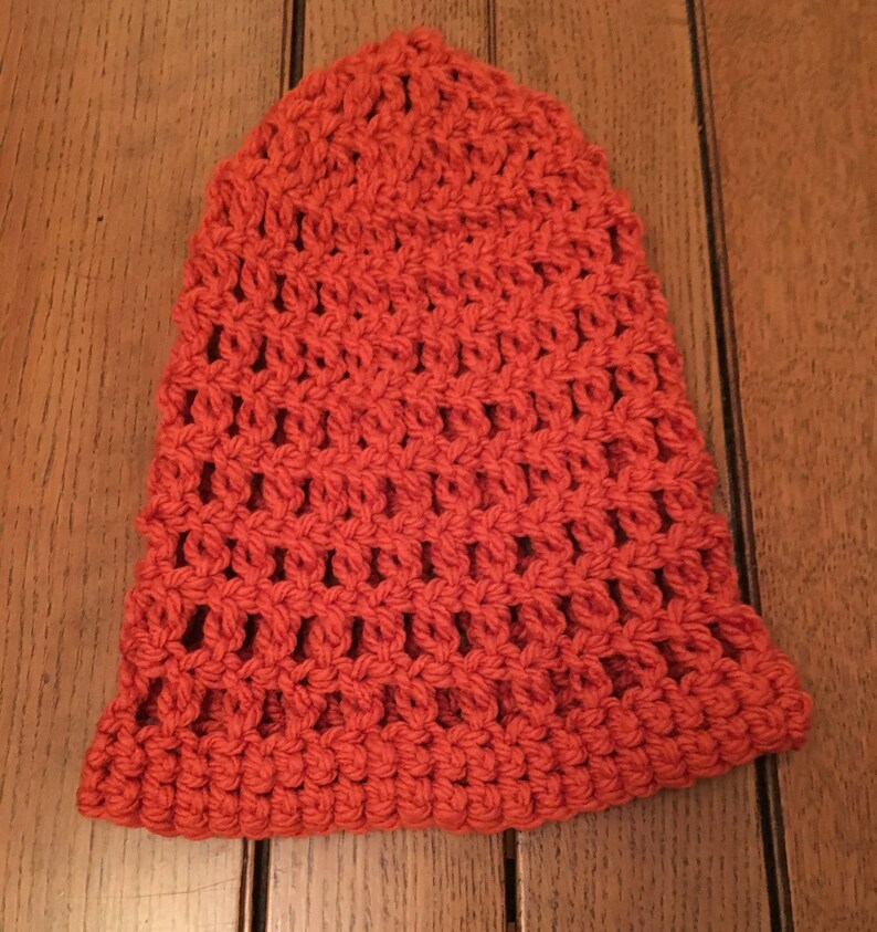 Puede incluir: Un gorro de punto de ganchillo de color naranja brillante. El gorro tiene un patr&oacute;n de punto simple y abierto.