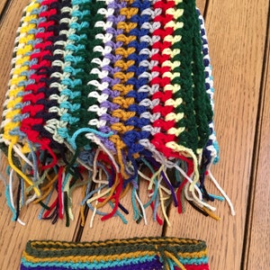 May include: A colorful crocheted scarf with fringe and a matching crocheted headband. The scarf is made with a variety of colors, including red, yellow, blue, green, and white.