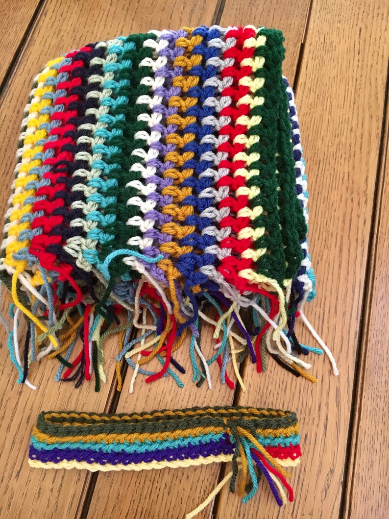 May include: A colorful crocheted scarf with fringe and a matching crocheted headband. The scarf is made with a variety of colors, including red, yellow, blue, green, and white.