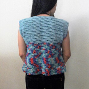 May include: A sleeveless crocheted vest with a blue top and a colorful geometric pattern on the bottom.