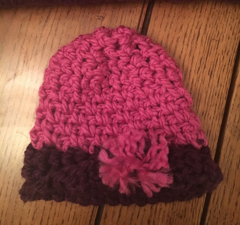 May include: A pink and purple crocheted hat with a fluffy pom-pom.