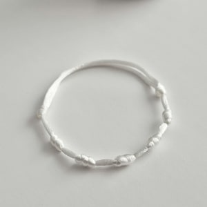 Peut inclure: Un bracelet en cordon blanc composé d'une série de petits nœuds régulièrement espacés le long du fil. Le bracelet est fabriqué à partir d'une seule pièce continue de fil blanc fin et lisse, formant un design en boucle circulaire.