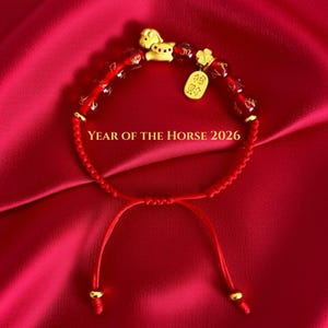 Peut inclure: Bracelet rouge à perles avec des détails dorés, comprenant un charm en forme de cheval et un pendentif en forme de pièce. Le bracelet est posé sur un fond de satin rouge, avec le texte "YEAR OF THE HORSE 2026".