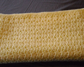 May include: A crocheted baby blanket in a pale yellow colour. The blanket has a delicate, lacy pattern.