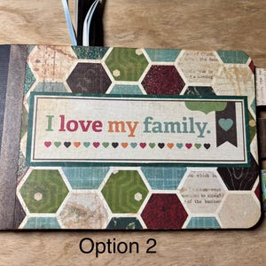 May include: A scrapbook with a patterned cover featuring a geometric design in shades of green, brown, and teal. The cover displays the text "I love my family" with colorful hearts. The spine is black, and the pages have tabs.