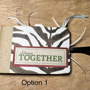 May include: A small, handmade scrapbook with a zebra print cover and the words "Always Together" on a rectangular label. The book has a tan spine, black ribbon, and decorative paper strips.