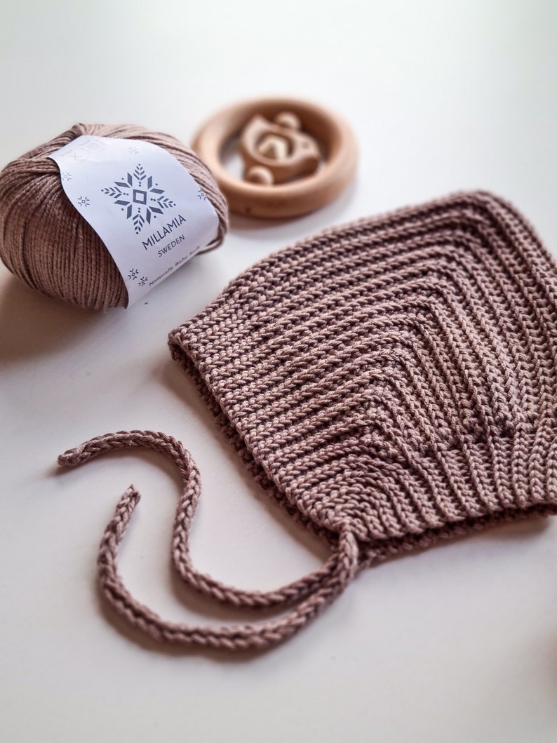 Pu&ograve; includere: Un berretto per neonato in crochet rosa chiaro con lacci abbinati. Il berretto &egrave; realizzato con una maglia testurizzata e ha una corona a punta. La matassa di lana &egrave; etichettata "MILLAMIA SWEDEN".
