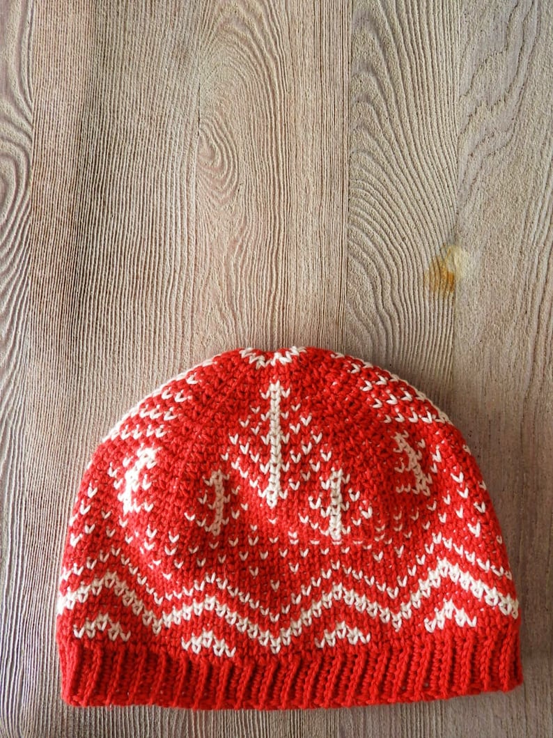 Puede incluir: Gorro de punto de crochet rojo y blanco con un patr&oacute;n geom&eacute;trico. El gorro est&aacute; hecho con un hilo suave y tiene una sensaci&oacute;n c&aacute;lida y acogedora.