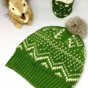 Puede incluir: Sombrero de punto verde con un patr&oacute;n geom&eacute;trico blanco y un pomp&oacute;n de piel sint&eacute;tica marr&oacute;n en la parte superior.