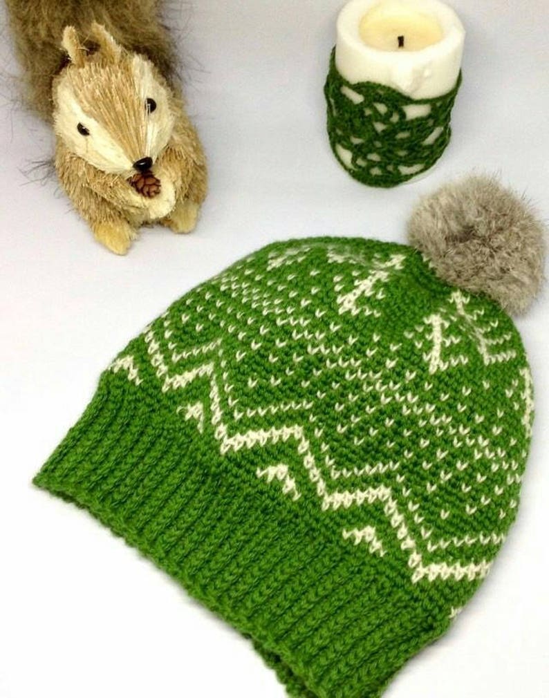 Puede incluir: Sombrero de punto verde con un patr&oacute;n geom&eacute;trico blanco y un pomp&oacute;n de piel sint&eacute;tica marr&oacute;n en la parte superior.