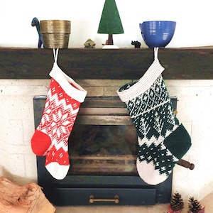 Puede incluir: Dos calcetines de Navidad de ganchillo colgados en una repisa de chimenea. El calcetín de la izquierda es rojo y blanco con un patrón de copo de nieve. El calcetín de la derecha es verde y blanco con un patrón geométrico.