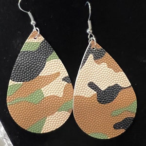 May include: A pair of teardrop-shaped earrings with a camouflage pattern in shades of brown, green, and black. The earrings have a textured, almost leather-like finish.