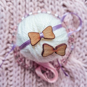 May include: Two wooden bow tie shapes with a purple ribbon wrapped around a ball of white yarn.