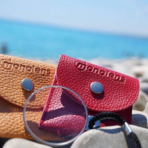 May include: Two small leather cases with a magnifying glass. The cases are tan and red and have the word "monolens" embossed on them.