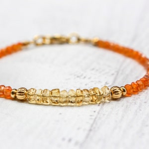 Puede incluir: Una delicada pulsera con pequeñas piedras preciosas de color naranja y amarillo. La pulsera tiene un cierre y detalles dorados. Las piedras están dispuestas en un patrón lineal, creando un diseño simple pero elegante. La pulsera es adecuada para el uso diario.