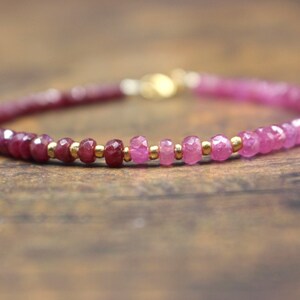 May include: A delicate bracelet featuring faceted ruby beads in varying shades of pink and red. The beads are interspersed with small gold-colored beads. The bracelet is secured with a gold-colored clasp.