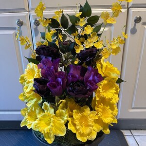 May include: A black planter with a yellow and purple flower arrangement. The flowers are in full bloom and have a variety of textures.