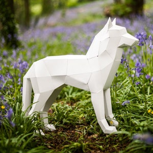 May include: A white paper wolf sculpture standing in a field of purple flowers. The sculpture is made of folded paper and has a realistic appearance.