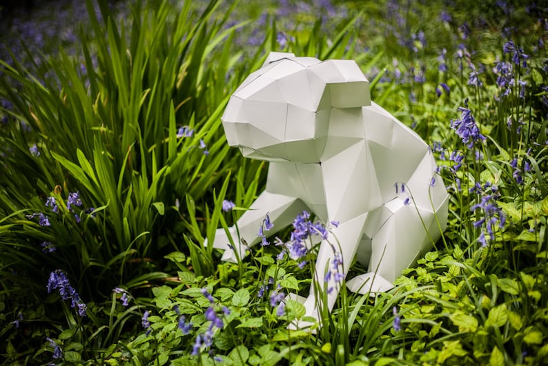 May include: A white origami sculpture of a koala sitting in a bed of bluebells. The sculpture is made of paper and has a geometric design.