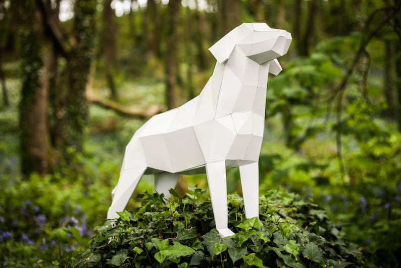 Puede incluir: Una escultura de perro de papel blanco y geom&eacute;trico que se encuentra en un entorno de bosque verde y frondoso.