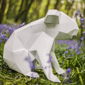 May include: A white paper origami koala sculpture sitting in a field of purple flowers.