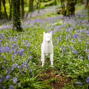 May include: A white origami wolf sculpture standing in a field of purple wildflowers