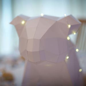 May include: A white paper sculpture of an animal, possibly a koala, with a geometric design. The sculpture is illuminated with small white lights.