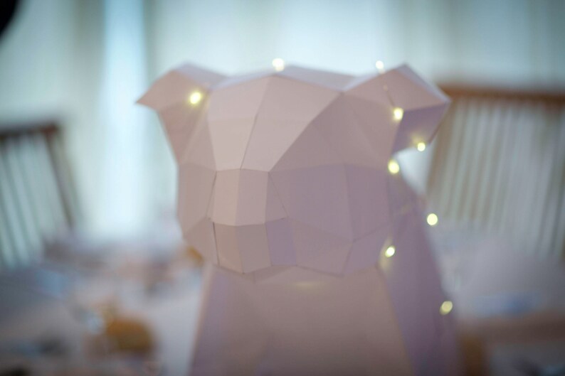May include: A white paper sculpture of an animal, possibly a koala, with a geometric design. The sculpture is illuminated with small white lights.
