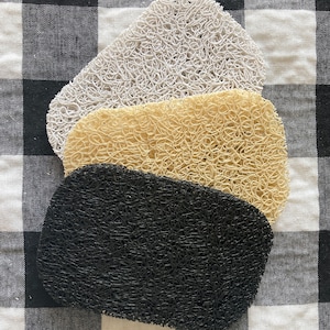 May include: Three textured soap saver pads in black, beige, and white. The pads are made of a woven material and are stacked on top of each other.