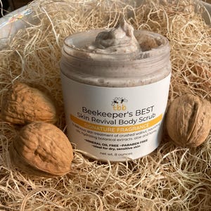 May include: A jar of Beekeeper's Best Skin Revival Body Scrub with the text "Signature Fragrance" and "net wt. 8 ounces." The jar is surrounded by three walnuts and straw.