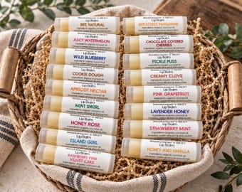 May include: A collection of twenty Beekeeper's BEST lip balm tubes arranged in a woven basket filled with shredded paper. Each cylindrical tube features a white label with black text listing ingredients and unique flavor names like Bee Natural.
