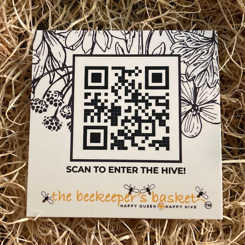 May include: A square, cream-coloured card with a large black and white QR code. The card features floral illustrations and the text "SCAN TO ENTER THE HIVE!" and "the beekeeper's basket" with bee graphics.