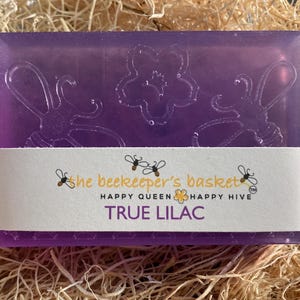 May include: A purple bar of soap with a floral design and the text "the beekeeper's basket" "HAPPY QUEEN HAPPY HIVE" "TRUE LILAC"
