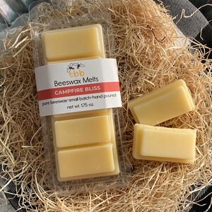 May include: A package of four beeswax melts in a clear plastic container. The label reads "tbb Beeswax Melts CAMPFIRE BLISS pure beeswax-small batch-hand poured net wt. 1.75 oz."