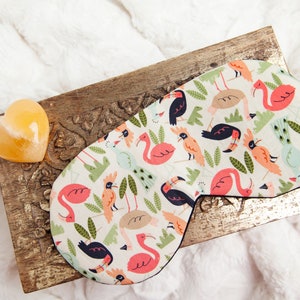 May include: A white sleep mask with a colorful pattern of pink flamingos, toucans, and peacocks on a green leafy background.