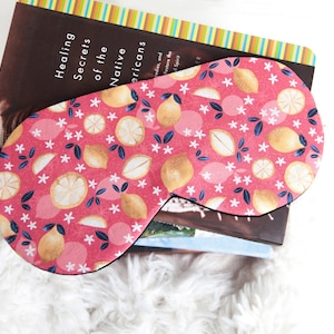 May include: A pink sleep mask with a lemon and flower pattern. The mask is on top of a stack of books. The book on top has the title "Healing Secrets of the Native Americans".