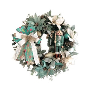 May include: A teal and gold Christmas wreath with a nutcracker figurine, white poinsettias, and a green and gold bow.