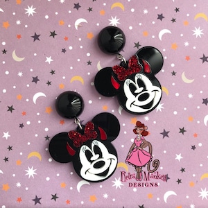 May include: A pair of black and white Minnie Mouse earrings with red glitter bows. The earrings are dangle style with black round tops.