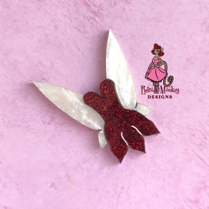 May include: Red glitter fairy wings with white iridescent wings. The wings are attached to a red glitter body. The wings are in a flying position. The wings are made of a thick, durable material. The wings are perfect for adding a touch of whimsy to any outfit.