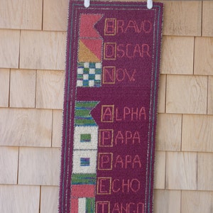 Puede incluir: Una pared de tela color marrón con una serie de cuadrados y rectángulos coloridos. Cada cuadrado tiene una letra dentro y una palabra debajo. Las palabras son: BRAVO, OSCAR, NOV, ALPHA, PAPA, PAPA, ECHO, TANGO, INDIA, TANGO.