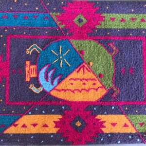 May include: A rectangular, purple rug with a geometric design. The rug features a central circular motif divided into sections of blue, green, and orange. The border includes pink, teal, and green geometric patterns. The rug's dimensions are not visible.