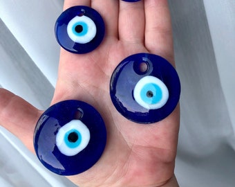 May include: Four blue glass evil eye charms of different sizes with white and light blue centers. The charms are round and have a hole at the top for hanging.