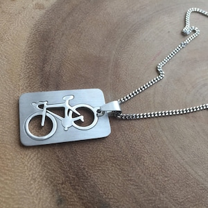 May include: A silver chain necklace with a pendant shaped like a bicycle. The pendant is cut out of metal, creating a silhouette of a bicycle.