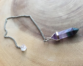 Pode incluir: Uma corrente de prata com um pêndulo de cristal roxo e verde e um pequeno cristal transparente na ponta.