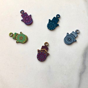 May include: Five hamsa hand charms with different colourful mandala patterns. The charms are made of metal and have a hole at the top for hanging.