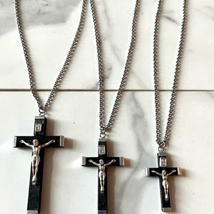May include: Three silver chain necklaces with black wooden crucifix pendants. The crucifixes feature a silver Jesus figure and are different sizes.