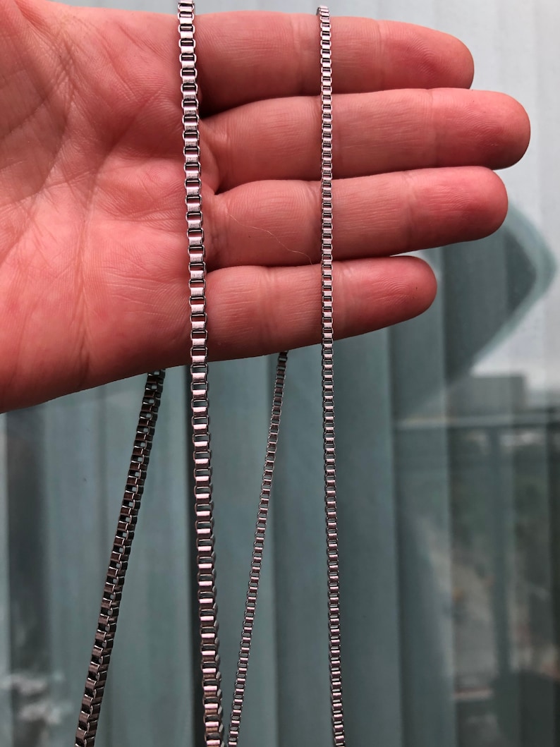 May include: Three silver chains of different lengths, shown against a blurred background.